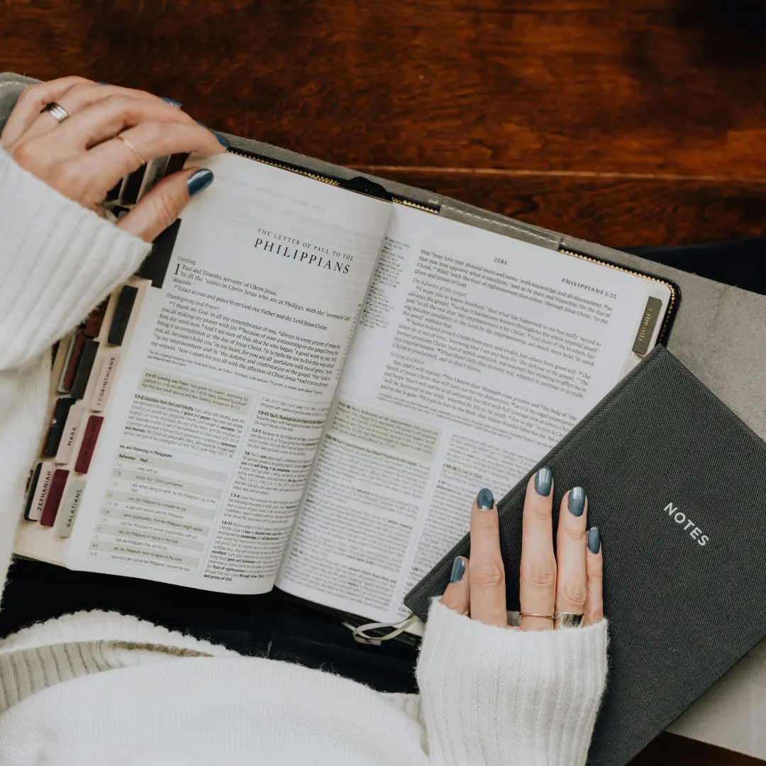 Woman doing personal Bible study with open Bible and notes on wooden table during quiet time